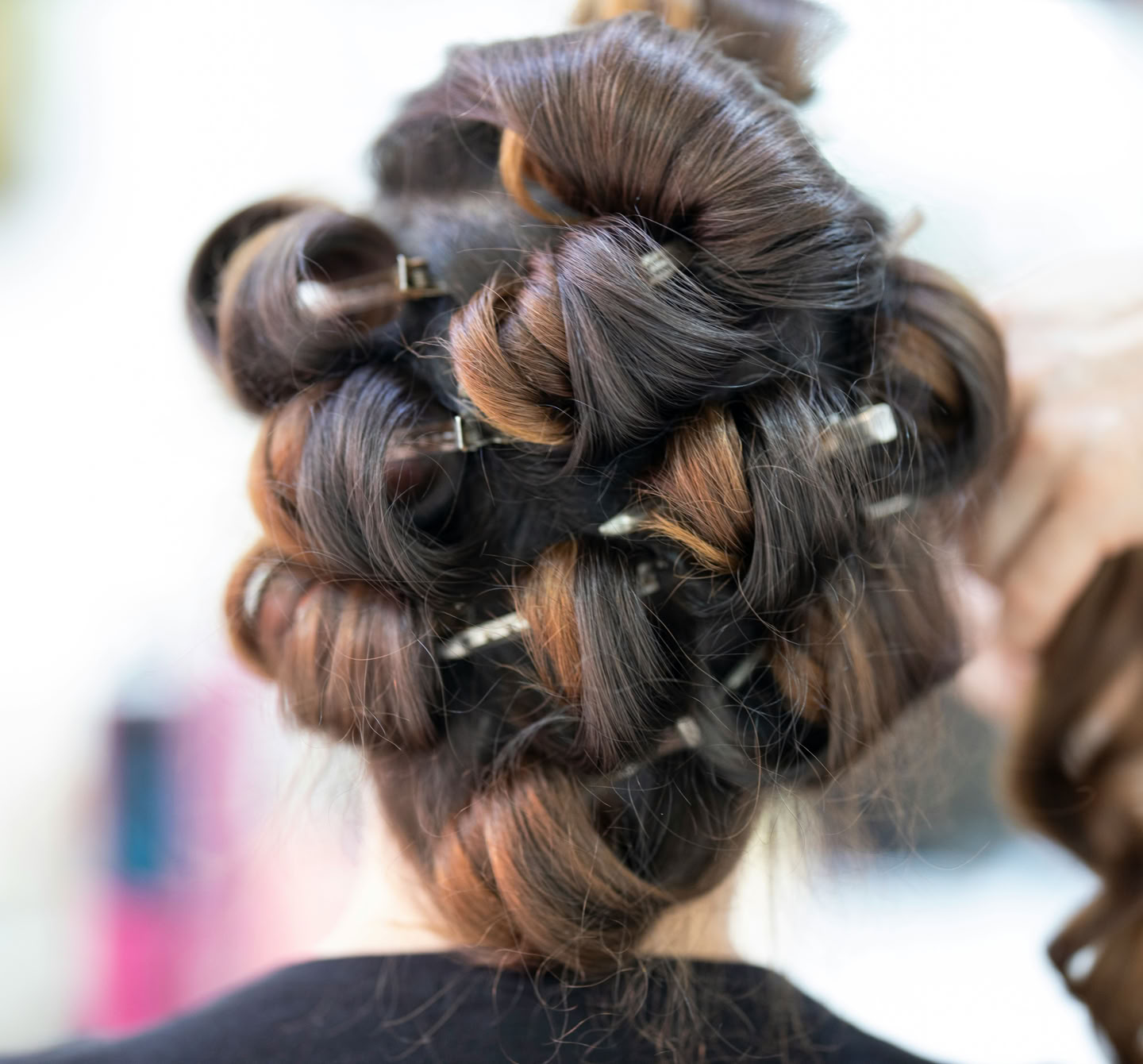 Hair styled in large curls with pins, viewed from the back, with a hand holding a section of hair.